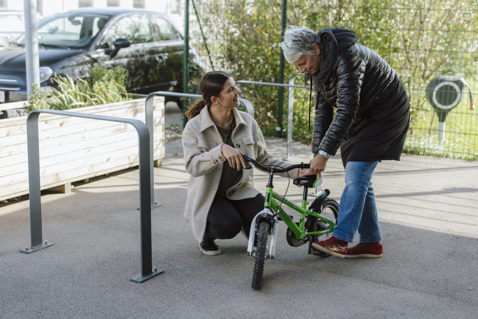 Auf dem Bild sind eine ältere Damen und ein junges Mädchen zusehen, die beide ein grüner Kinderfahrrad begutachten.