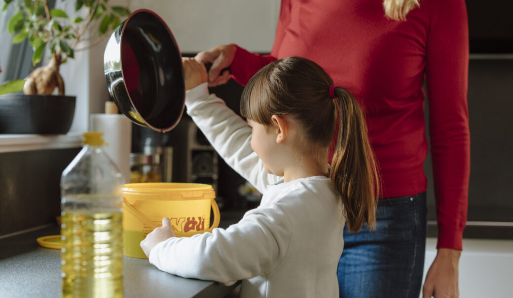 Das Bild zeigt eine Mutter mit ihrer Tochter, die gebrauchtes Speiseöl in einen gelben Behälter umfüllen.