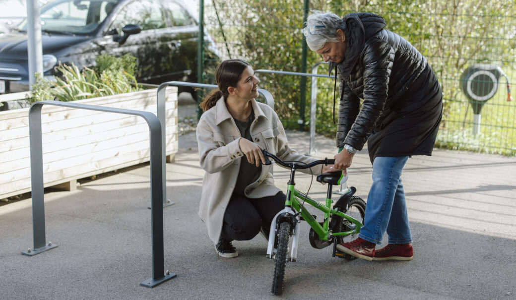 Auf dem Bild sind eine ältere Damen und ein junges Mädchen zusehen, die beide ein grüner Kinderfahrrad begutachten.